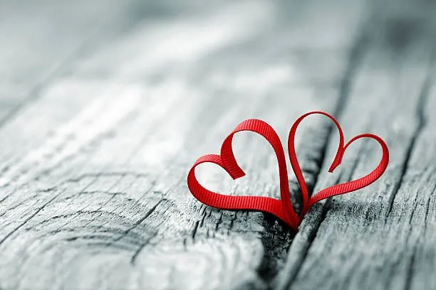 Image: Ribbons in heart shapes on a wooden surface.